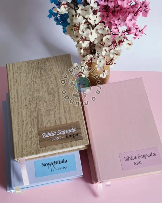 Duas Bíblias reformadas, uma com capa em textura de madeira clara e outra em rosa liso, sobre a mesa do ateliê