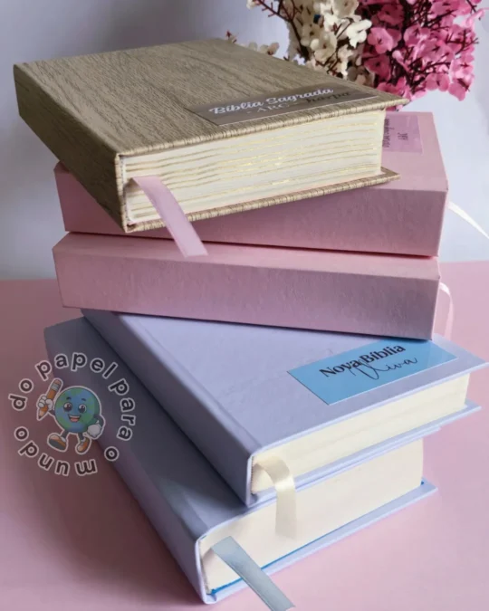 Pilha de quatro Bíblias reformadas com capas em bege, rosa e lilás, mostrando a lombada e o acabamento das bordas