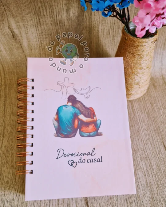 Caderno Devocional do Casal com espiral rosé e capa rosa ilustrada com um casal abraçado diante de uma cruz